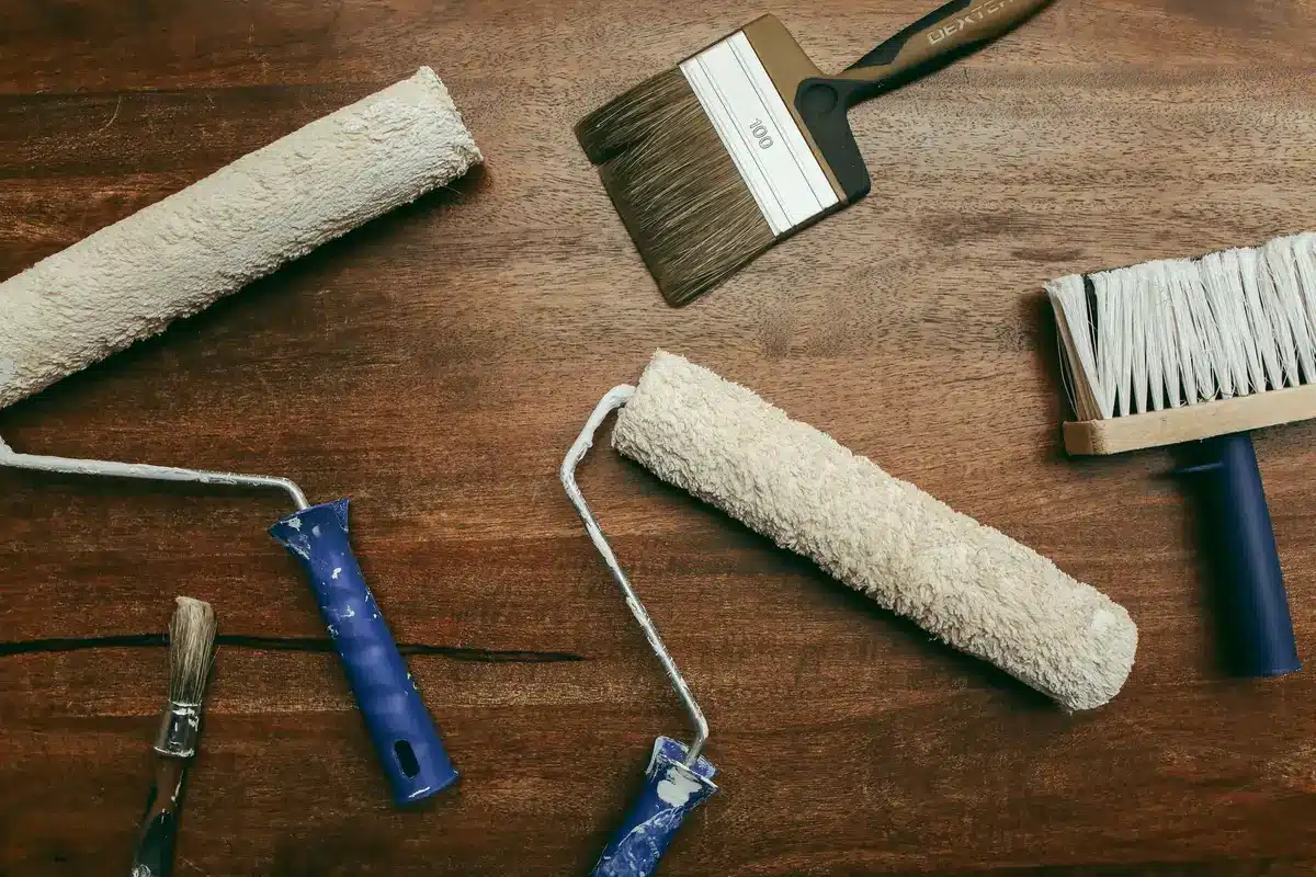 Outils de peinture professionnels : rouleau laqueur, pinceau plat et mini-rouleau mousse posés sur une surface de travai